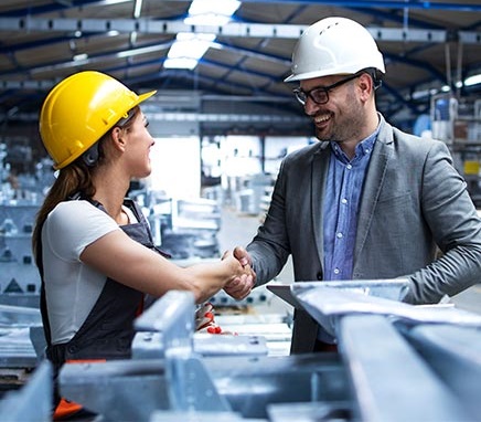 Dwóch inżynierów podaje sobie ręce w hali przemysłowej.